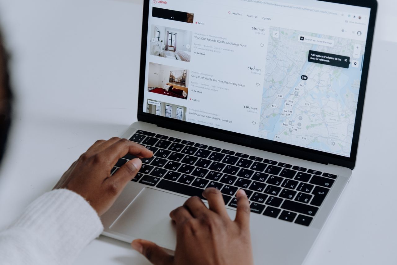 expertise-01 Hands typing on laptop searching Airbnb for accommodation options with map view.